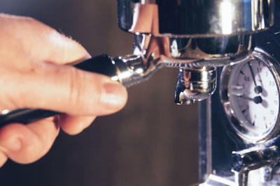 Close-up of hand holding portafilter by espresso maker at cafe