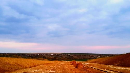 Dirt road amidst field against sky