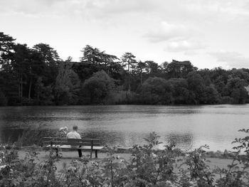 Rear view of men sitting by lake against sky