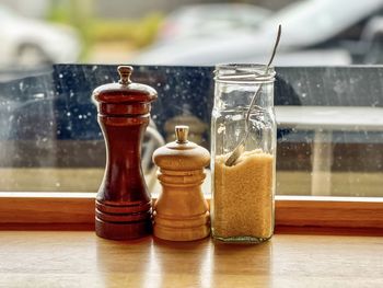 Close-up of salt and pepper shakers and sugar in jar on countertop against window view of sidewalk.
