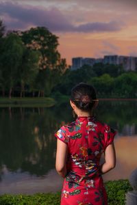 Rear view of young woman standing by lake during sunset