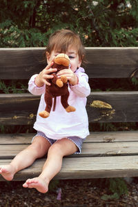 Cute baby girl holding stuffed toy while sitting at park