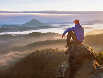 Sitting man on sharp rocky edge, enjoy amazing birds view. misty fall landscape bellow.