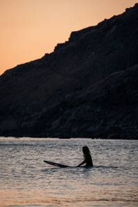 Silhouette man in sea against sky during sunset