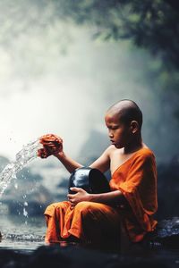 Rear view of boy sitting on glass against water