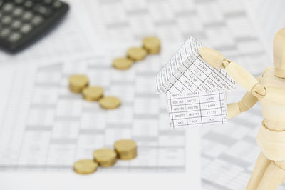 Close-up of wooden figurine with papers by coins on table