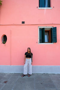 Full length portrait of smiling woman standing against building