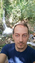 Portrait of young man standing against trees