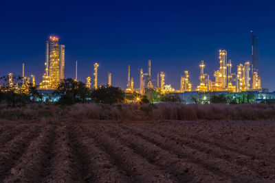 Illuminated factory by building against sky at night