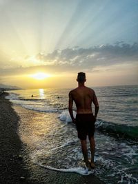 Rear view of man standing on beach at sunset