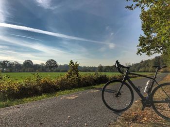 Bicycle on road amidst field against sky