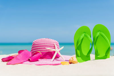 Close-up of flip-flop and hat at beach against sky during sunny day