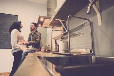 Man sitting by pregnant woman on kitchen counter at home