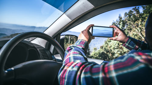 Cropped image of man photographing with mobile phone from car