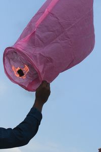 Low angle view of hand holding paper lantern against clear sky