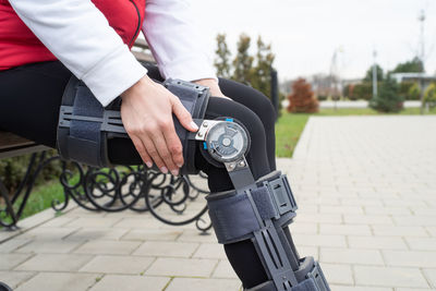 Woman wearing sport clothes and knee brace or orthosis after leg surgery, walking in the park.