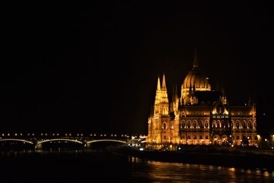 Illuminated building by river against sky at night
