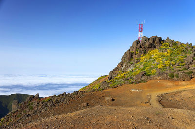 Communications tower on mountain by clouds against blue sky