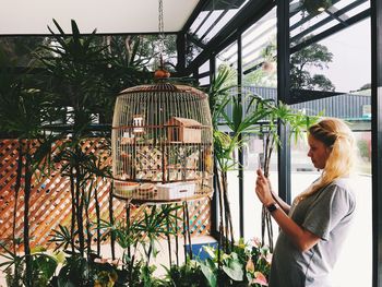 Woman photographing birdcage against plants