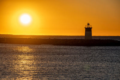 Lighthouse by sea against sky during sunset