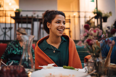 Smiling young woman looking away while sitting at table during dinner party