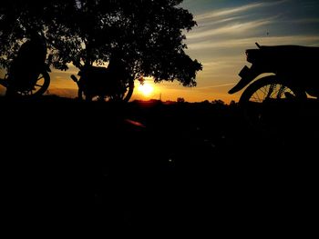 Silhouette of bicycle on field against sky at sunset