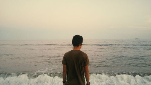 Rear view of man standing at beach against sky at dusk