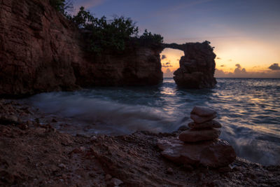 Rock formation on beach against sky during sunset