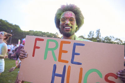 Portrait of smiling man holding free hugs sign against sky at carnival