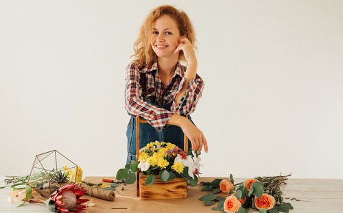 Portrait of smiling young woman with flowers in vase on table