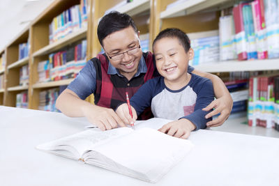 Smiling teacher assisting boy in writing at library