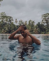 Shirtless man swimming in pool against sky
