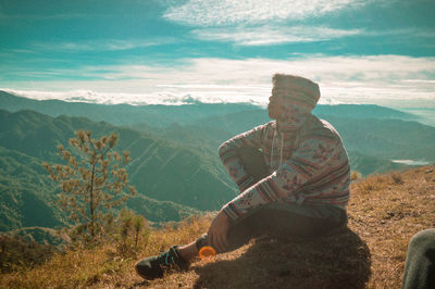 Man sitting on mountain against sky