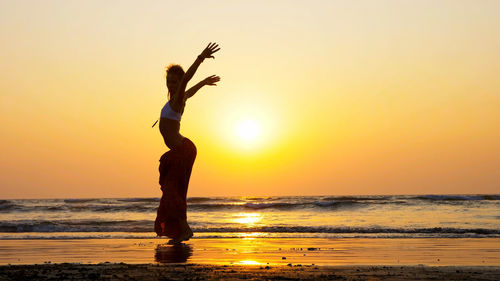 Full length of woman jumping on beach during sunset