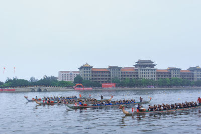 People on boats in river by city against clear sky