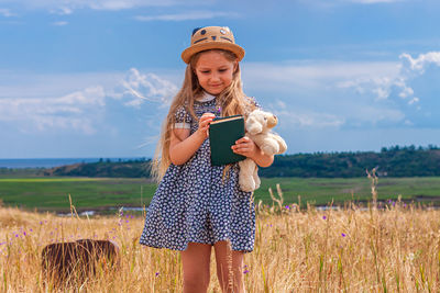 Child girl in straw hat dress sitting vintage suitcase reading book cute kid toy looking at notebook