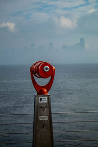 Coin operated telescope by sea against sky