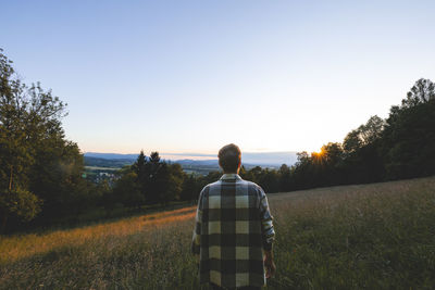 Rear view of man standing on field against clear sky