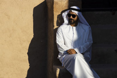 Man wearing sunglasses sitting against wall