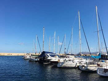 Sailboats moored on sea against clear blue sky