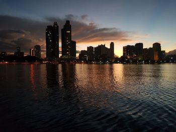 Sea by illuminated buildings against sky during sunset