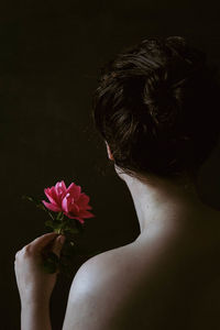 Close-up of woman with pink flower against black background