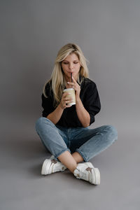 Portrait of young woman sitting against wall