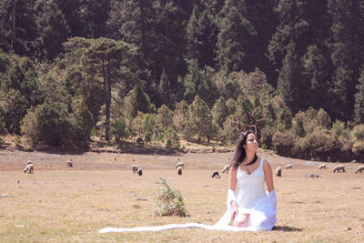 Woman with antler on hair in white dress sitting on field