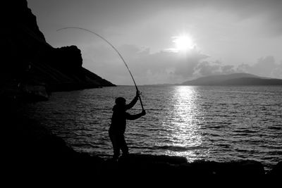 Silhouette man fishing in sea against sky