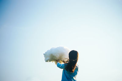 Girl holding up cloud against clear sky