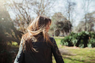 Rear view of mid adult woman with brown hair standing against trees in park