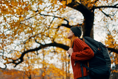 Rear view of woman standing on tree during autumn