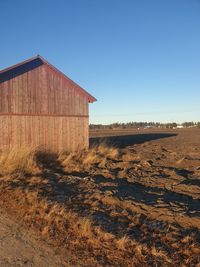 Barn on field against clear blue sky