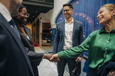 Happy businesswomen shaking hands by male colleagues in hotel lounge